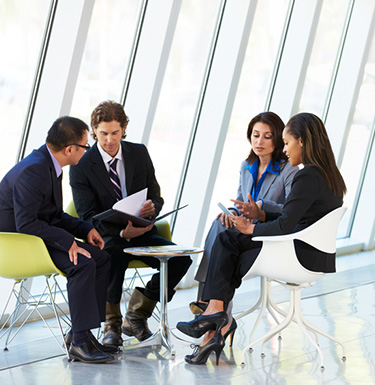 Four business people sit around a small table discussing documents